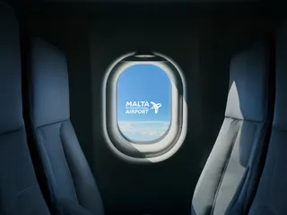 View through an aircraft cabin window showing the Malta International Airport logo