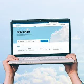 Hands holding a laptop against a blue sky, showing the Malta International Airport Flight Finder