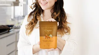 Woman holding a pouch of Cupio snacks in a bright kitchen