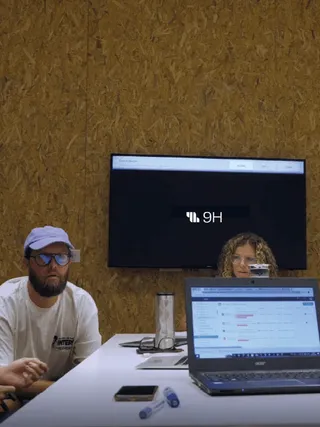 9H team meeting: a bearded man in a cap, a laptop and a wall screen showing the 9H logo